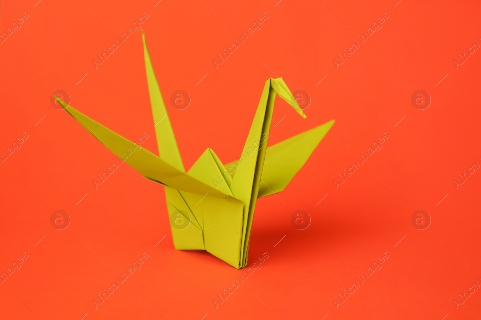 Photo of Origami art. Handmade paper crane on orange background, closeup