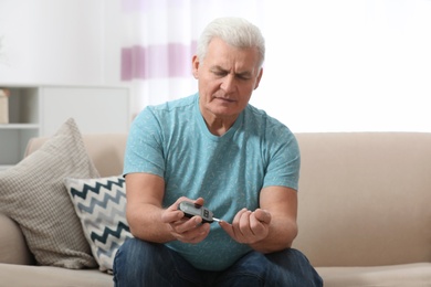 Photo of Senior man using digital glucometer at home. Diabetes control