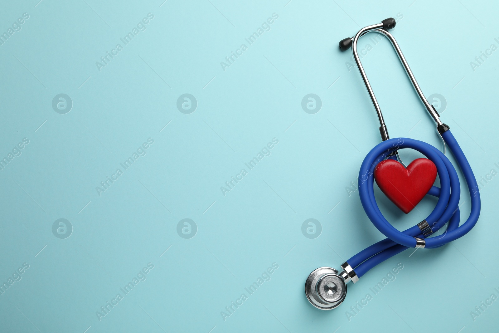 Photo of Stethoscope and red heart on light blue background, top view. Space for text