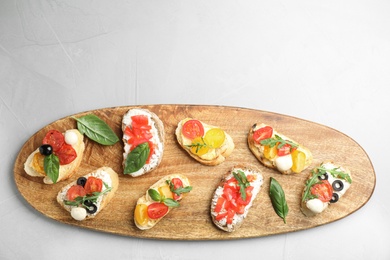 Wooden board with delicious tomato bruschettas on light grey background, top view