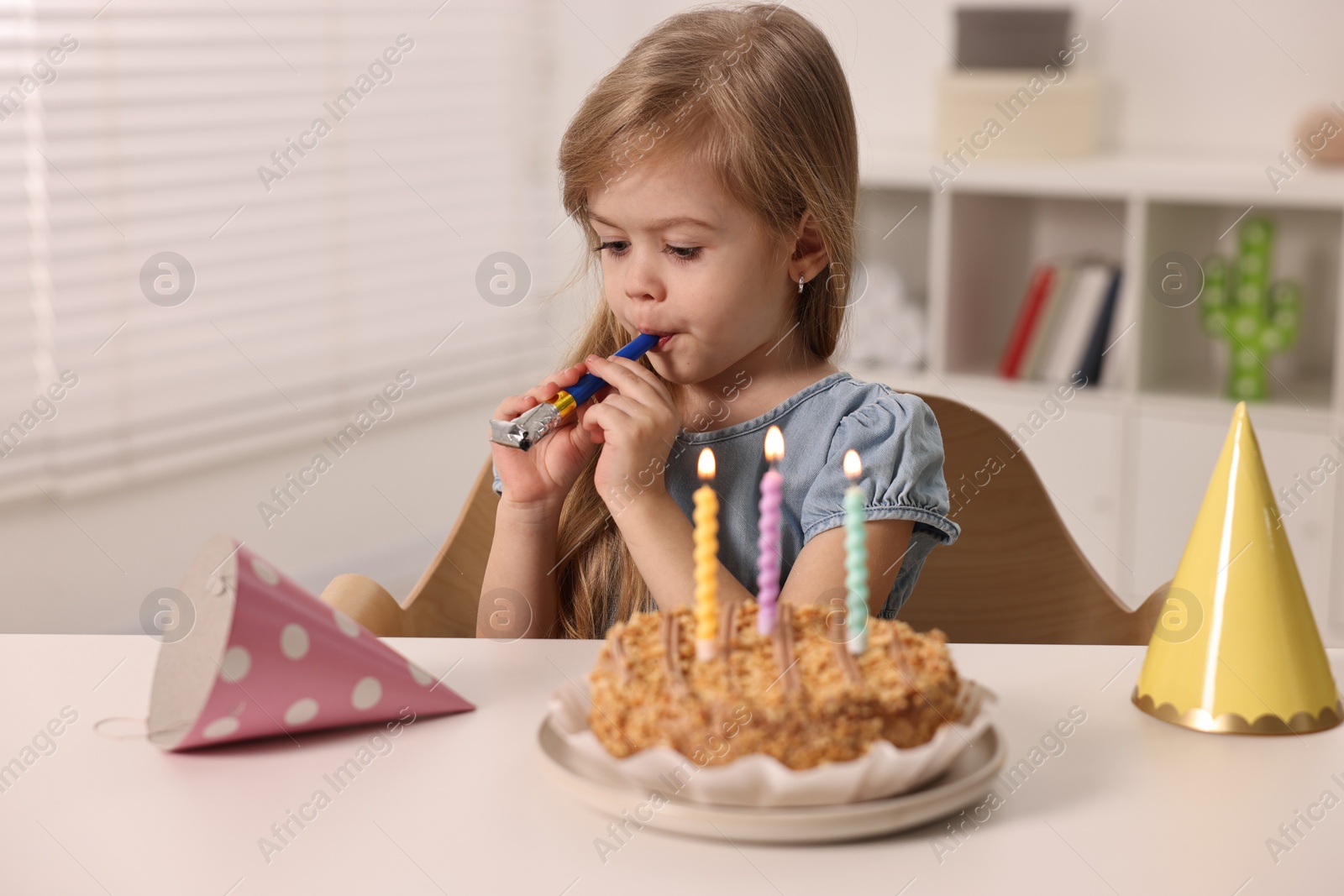 Photo of Birthday celebration. Cute girl holding blower at table with tasty cake indoors