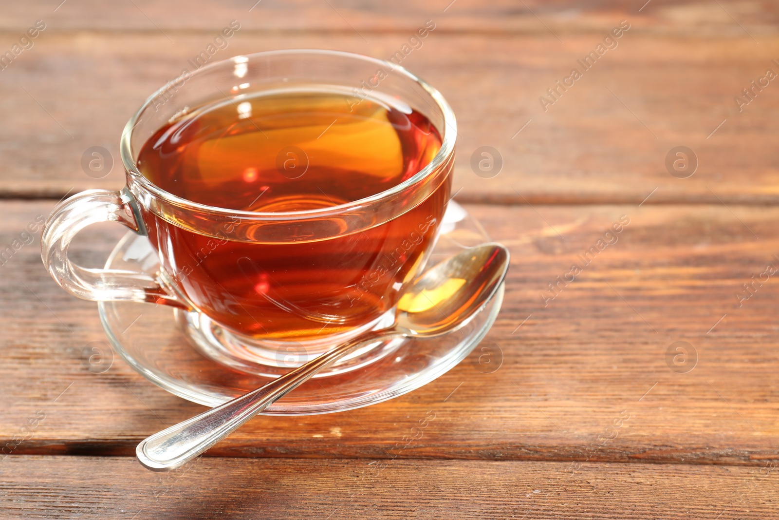 Photo of Glass cup of tea and spoon on wooden table