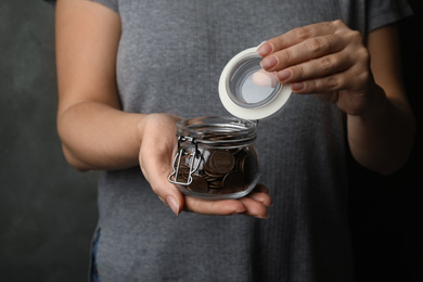 Photo of Woman holding glass jar with coins, closeup on hands