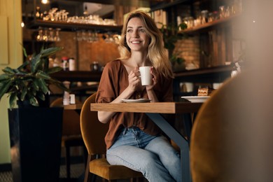 Photo of Young woman with cup of coffee at cafe in morning