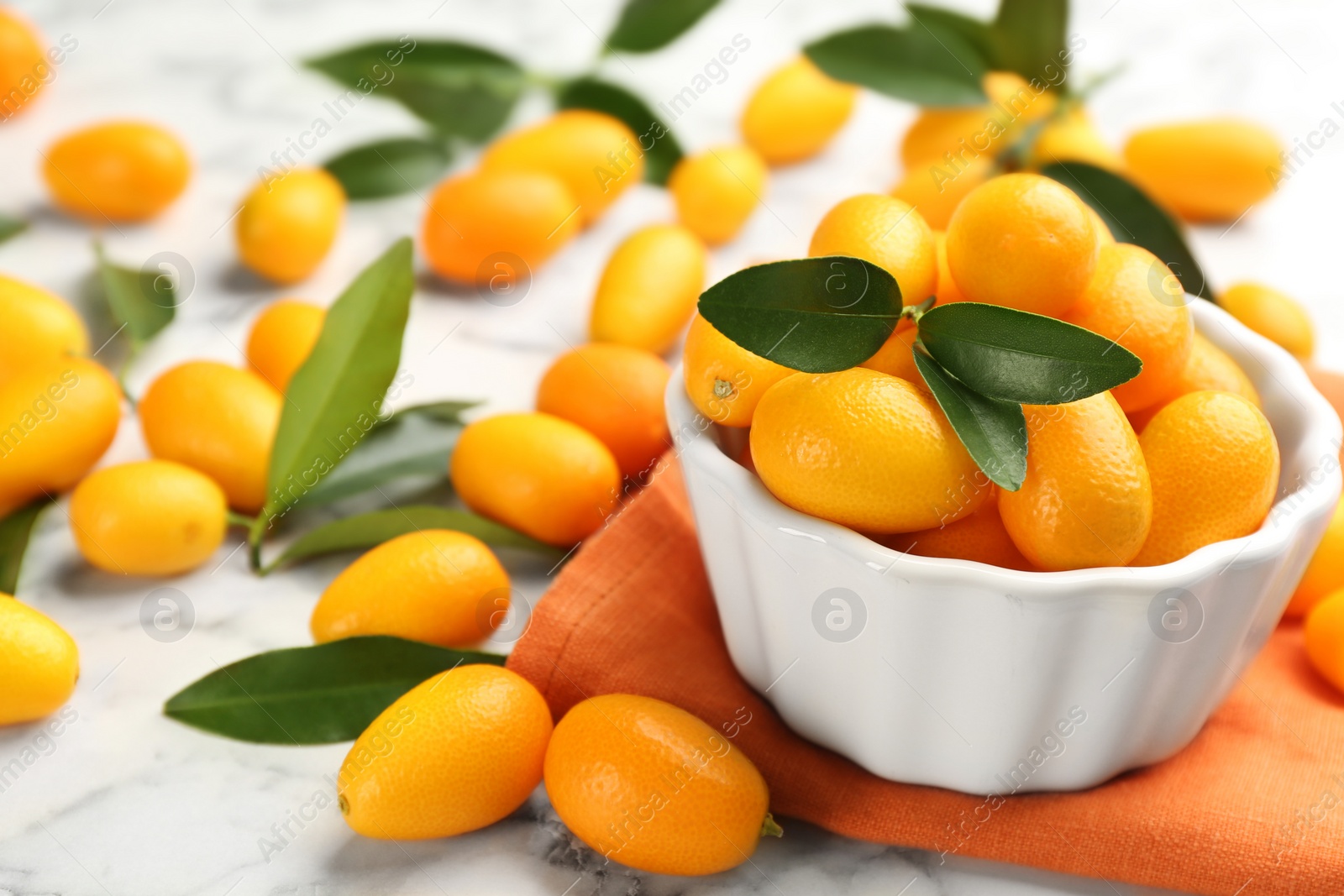 Photo of Fresh ripe kumquats in bowl on white marble table, space for text