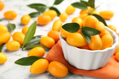 Photo of Fresh ripe kumquats in bowl on white marble table, space for text