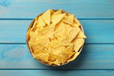 Tortilla chips (nachos) in bowl on light blue wooden table, top view