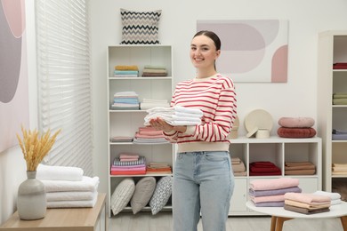Photo of Smiling young woman holding new towels in home textiles store