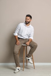 Photo of Handsome young man sitting on stool near beige wall