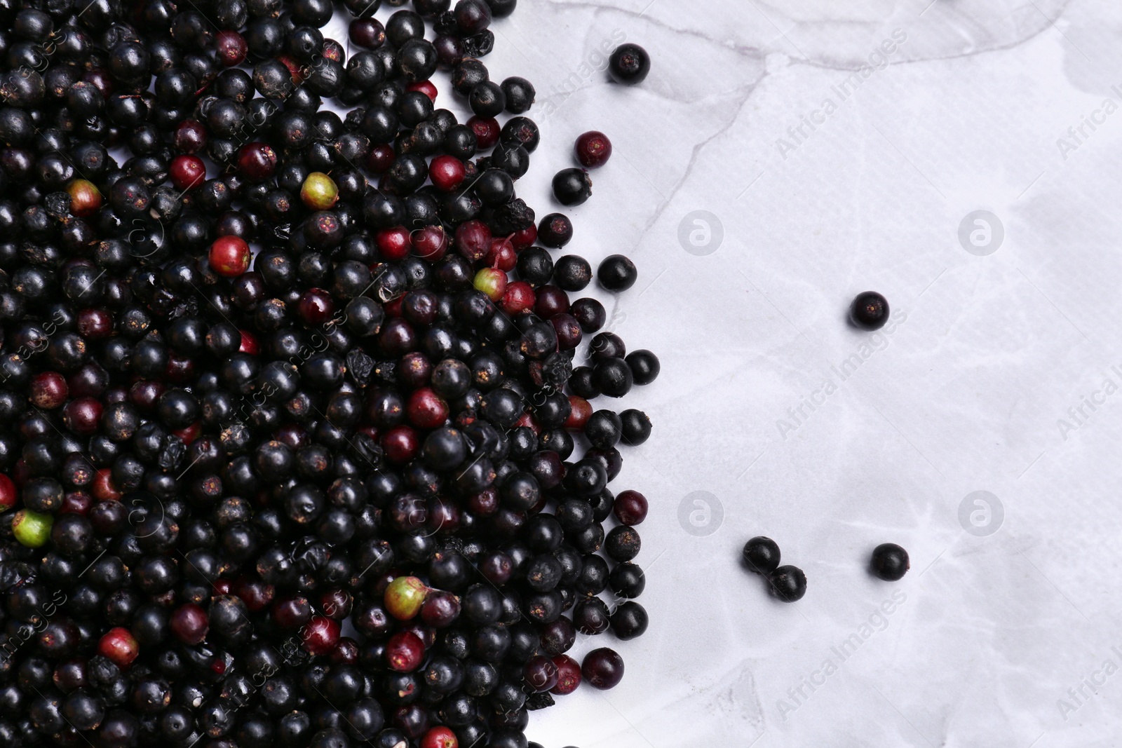 Photo of Pile of tasty elderberries (Sambucus) on white marble table, flat lay. Space for text