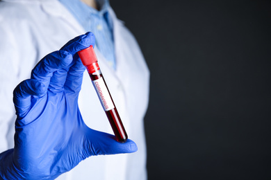 Photo of Scientist holding test tube with blood sample and label CORONA VIRUS on black background, closeup. Space for text