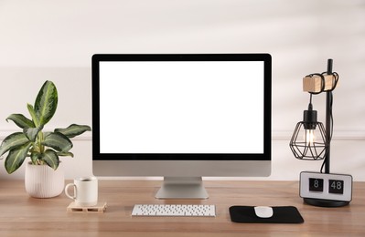 Photo of Modern computer with blank monitor screen and peripherals on wooden table indoors