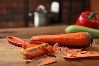 Photo of Carrot, peels and peeler on wooden table indoors, closeup