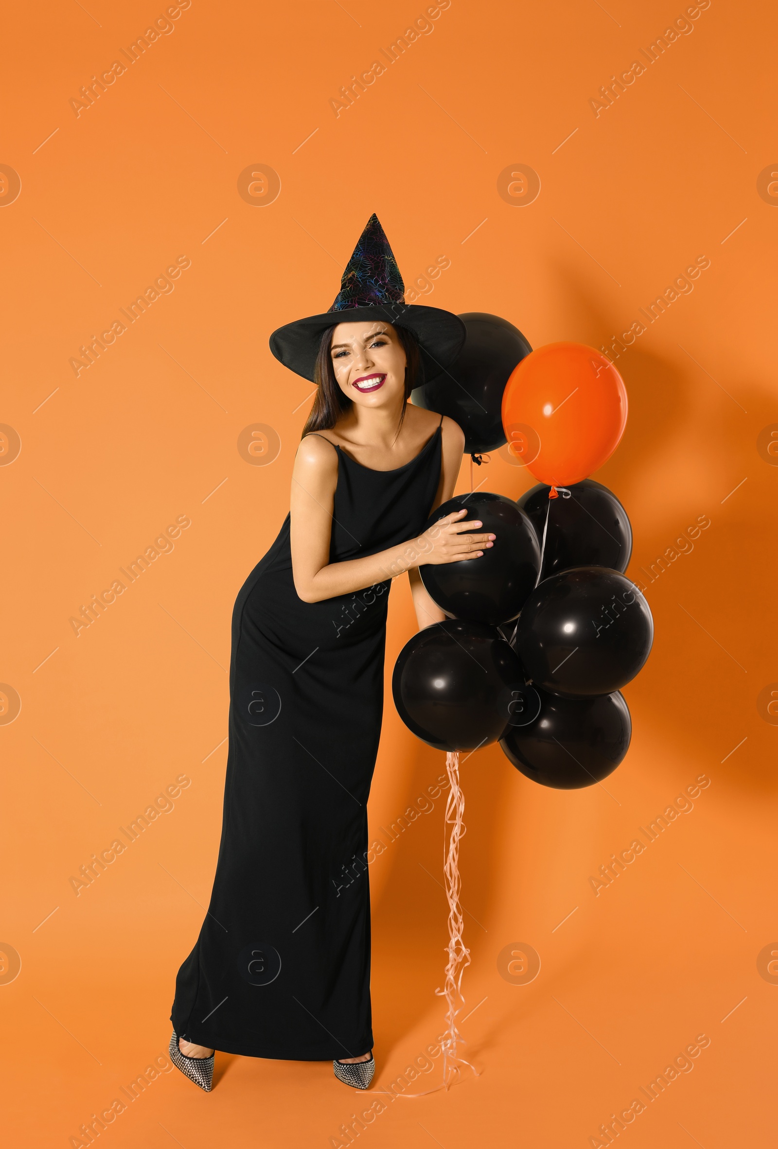 Photo of Beautiful woman wearing witch costume with balloons for Halloween party on yellow background