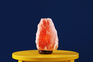 Himalayan salt lamp on yellow table against dark blue background