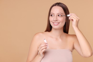 Beautiful woman applying serum onto eyelashes on beige background, space for text