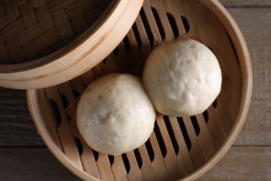 Photo of Delicious Chinese steamed buns in bamboo steamer on wooden table, top view