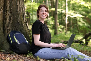 Smiling freelancer working with laptop in forest. Remote job