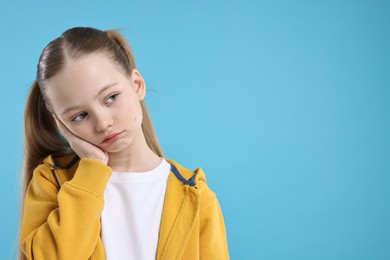 Portrait of sad girl on light blue background, space for text