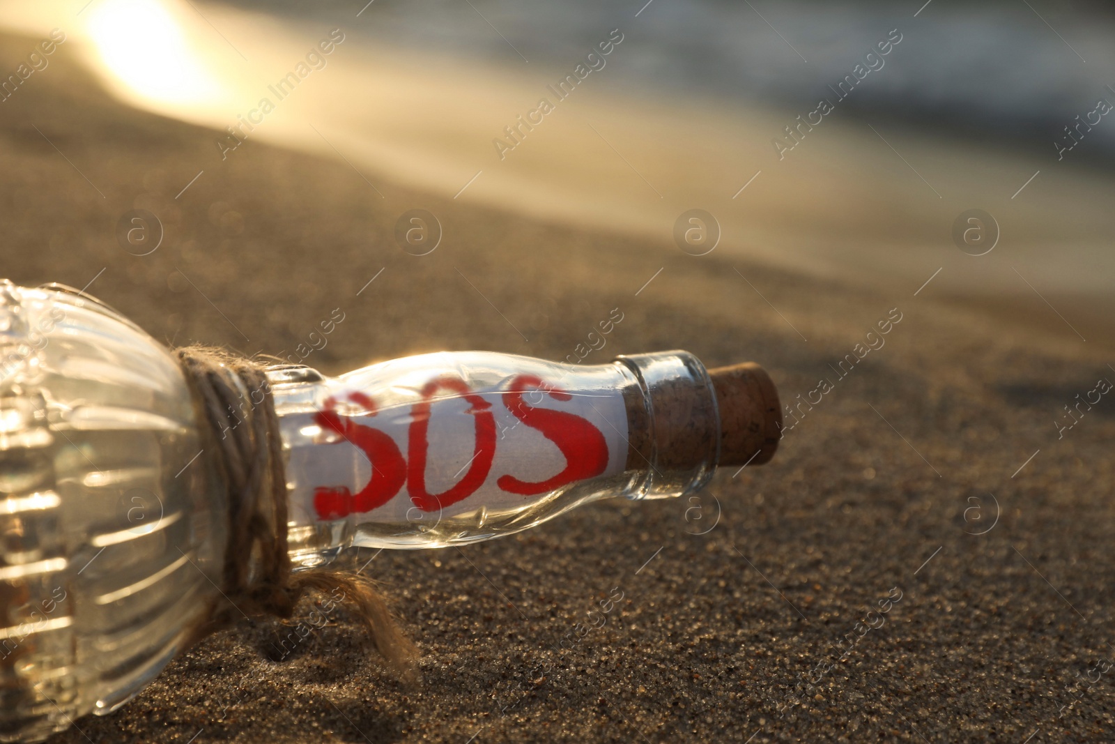 Photo of Glass bottle with SOS message on sand near sea, closeup