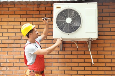 Photo of Male technician fixing air conditioner outdoors