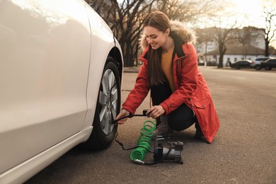 Photo of Young woman inflating car tire with air compressor on street