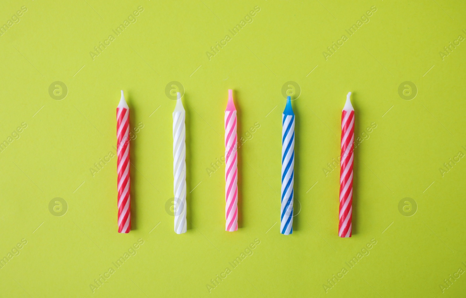 Photo of Colorful striped birthday candles on green background, top view