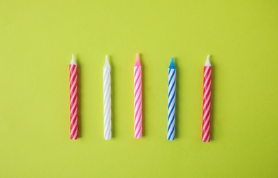 Colorful striped birthday candles on green background, top view
