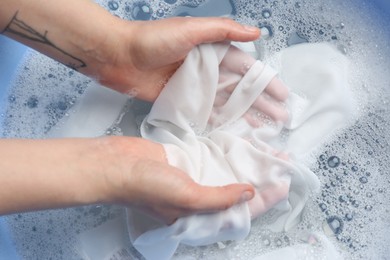 Top view of woman hand washing white clothing in suds, closeup