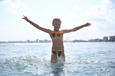 Photo of Happy little girl having fun in sea on sunny day. Beach holiday