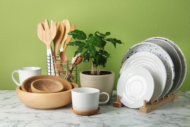 Photo of Potted plant and set of kitchenware on white marble table near green wall. Modern interior design