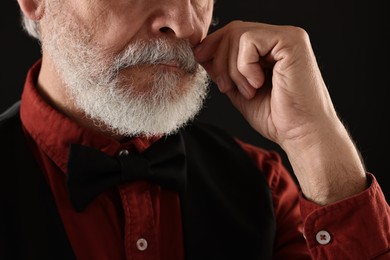 Photo of Man touching mustache on black background, closeup