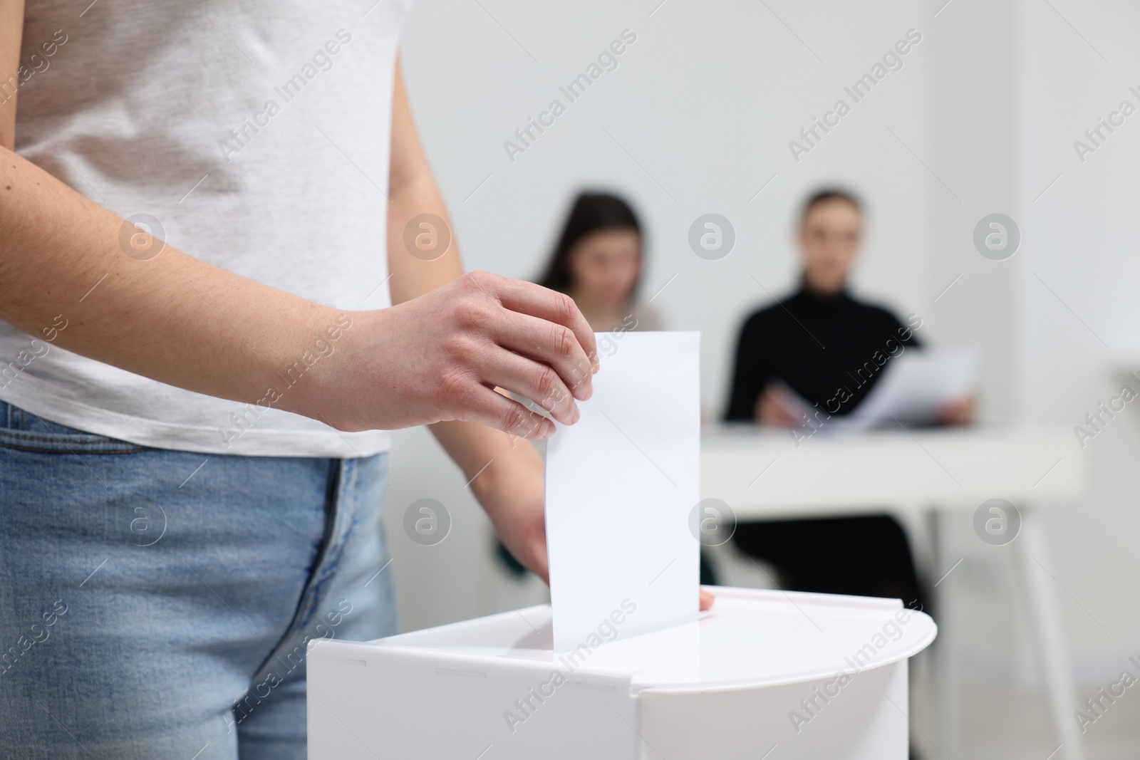 Photo of Woman putting her vote into ballot box on blurred background, closeup