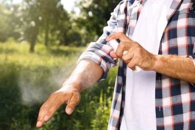 Photo of Man spraying tick repellent on arm during hike in nature, closeup