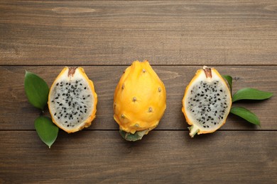 Photo of Delicious dragon fruits (pitahaya) and green leaves on wooden table, flat lay