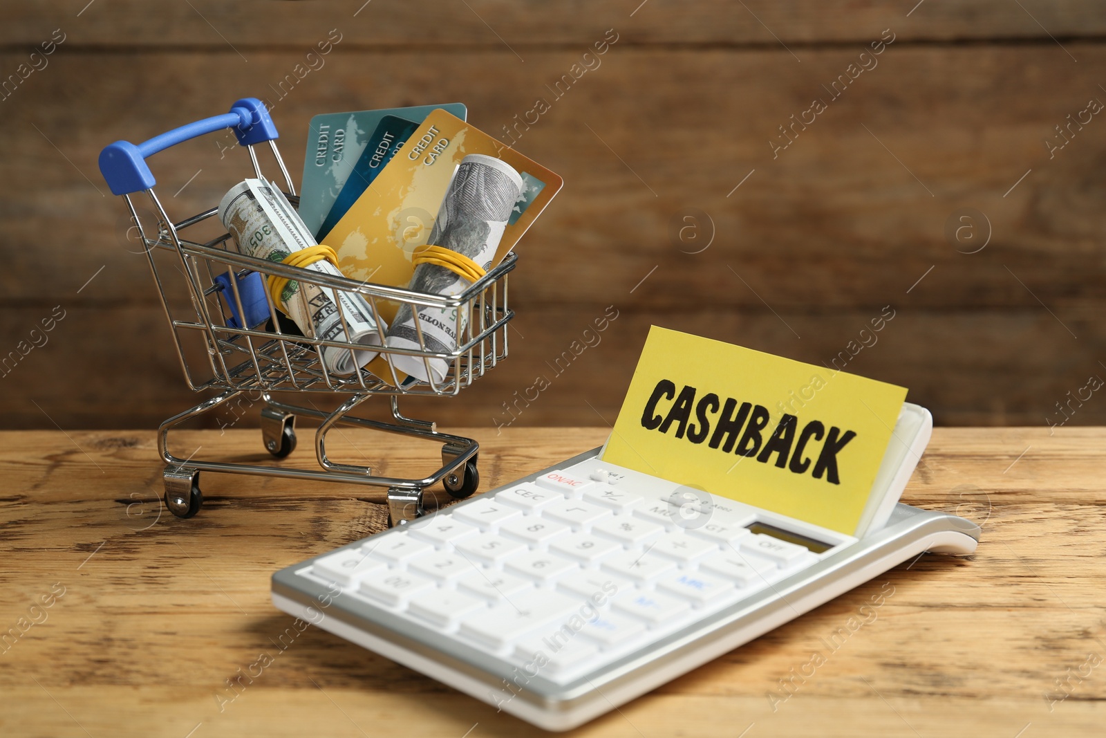 Photo of Calculator, shopping cart with rolled dollar banknotes and credit cards on wooden table. Cashback concept