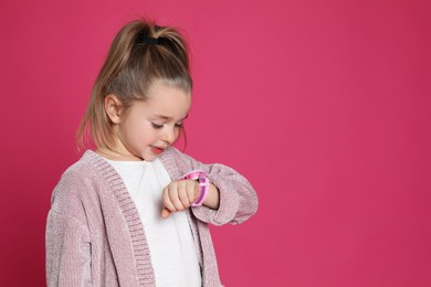 Photo of Little girl with smart watch on pink background, space for text
