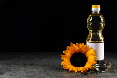 Photo of Bottle of sunflower cooking oil, seeds and beautiful flower on grey table against black background. Space for text
