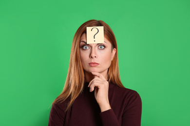 Photo of Pensive woman with question mark sticker on forehead against green background