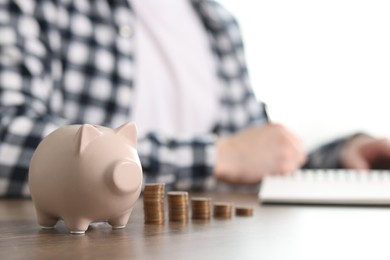 Photo of Financial savings. Man writing down notes at wooden table, focus on piggy bank