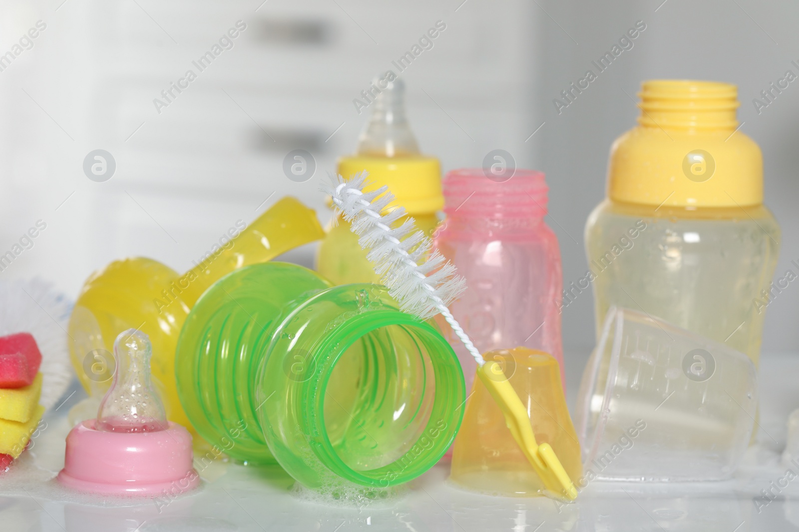 Photo of Clean baby bottles and nipples after sterilization near brush on white table, closeup