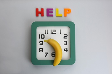 Photo of Clock with banana and word HELP on grey background, flat lay. Potency problem concept