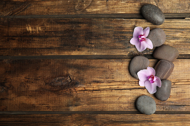 Photo of Stones with orchid flowers and space for text on wooden background, flat lay. Zen lifestyle