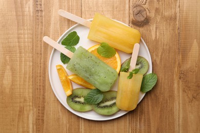 Photo of Plate of tasty orange and kiwi ice pops on wooden table, top view. Fruit popsicle