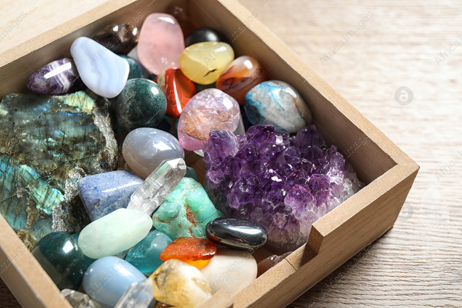 Photo of Box with different beautiful gemstones on wooden table