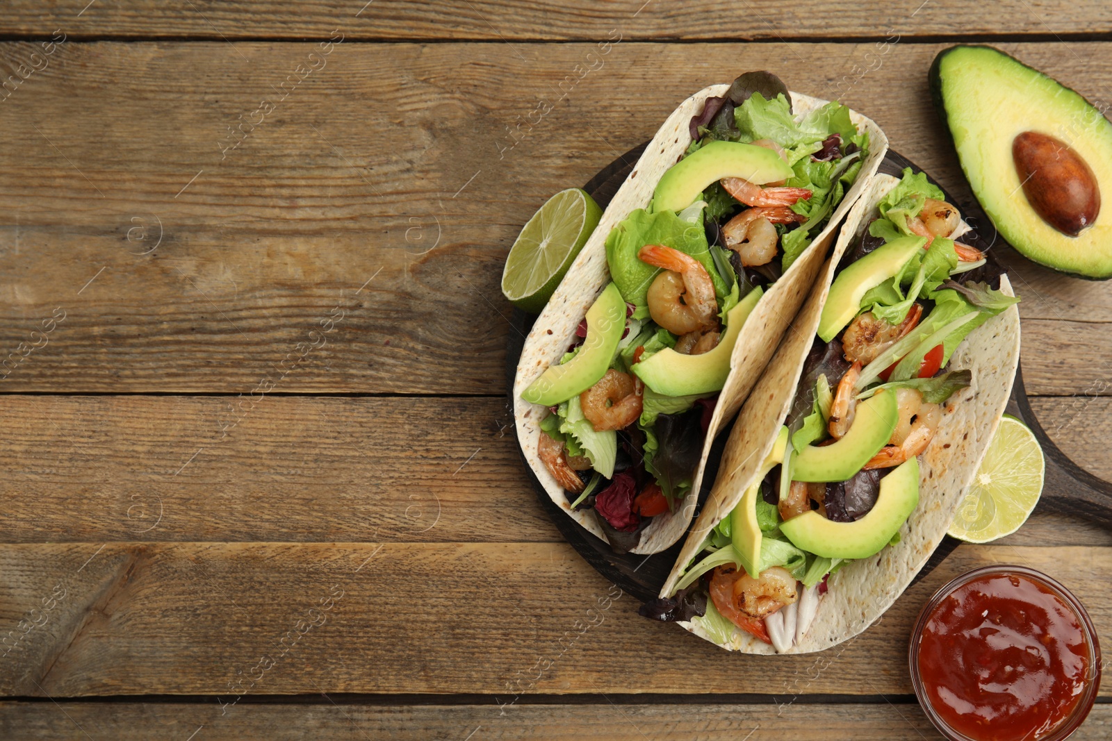 Photo of Delicious tacos with shrimps, avocado and sauce on wooden table, flat lay. Space for text