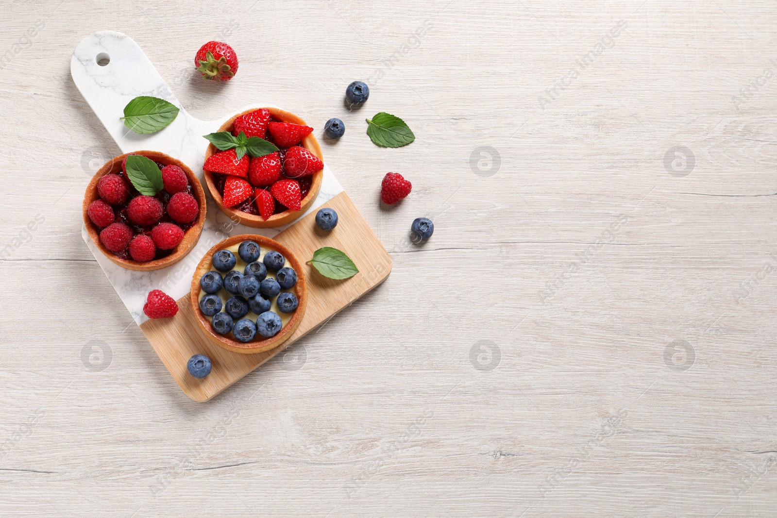 Photo of Tartlets with different fresh berries on light wooden table, flat lay and space for text. Delicious dessert