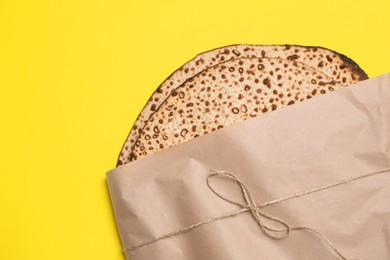 Photo of Tasty matzos wrapped with paper on yellow background, top view. Passover (Pesach) celebration