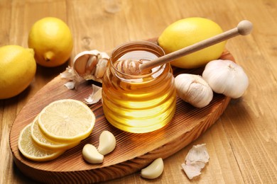 Photo of Jar with honey, garlic, lemons and dipper on wooden table