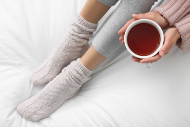 Photo of Woman with cup of tea wearing warm socks in comfortable bed, top view